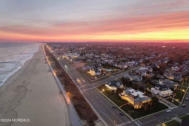 aerial view at dusk with a water view and a beach view