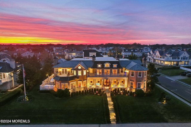 back house at dusk featuring a balcony and a lawn