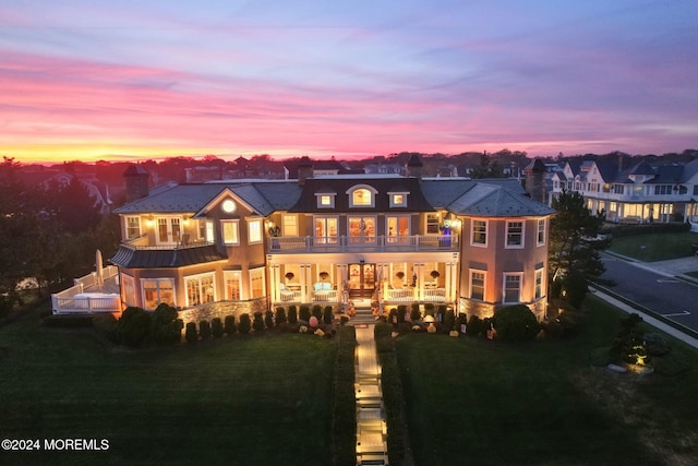 back house at dusk featuring a lawn and a balcony