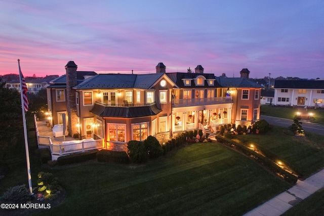 back house at dusk with a yard and a balcony