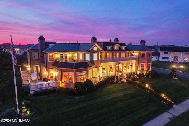 back house at dusk with a lawn and a balcony