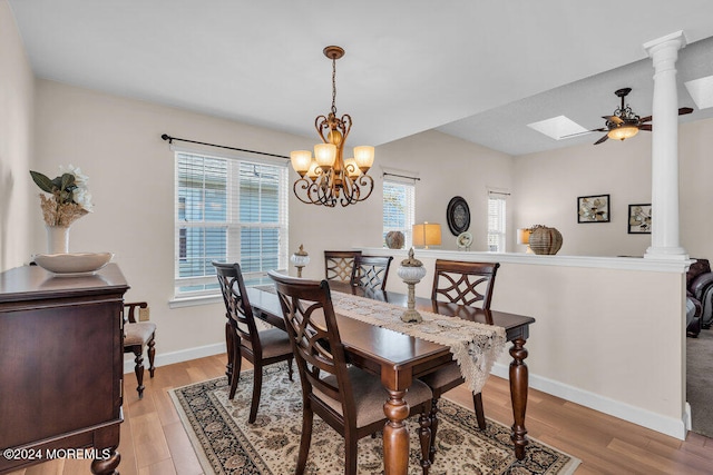 dining room with decorative columns, ceiling fan with notable chandelier, light hardwood / wood-style floors, and a skylight