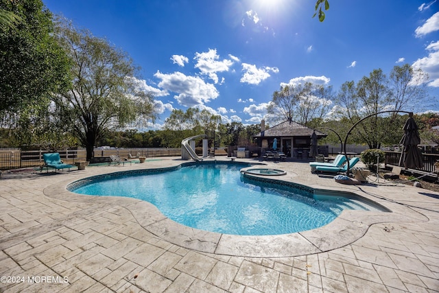 view of pool with a water slide, a patio, and an in ground hot tub