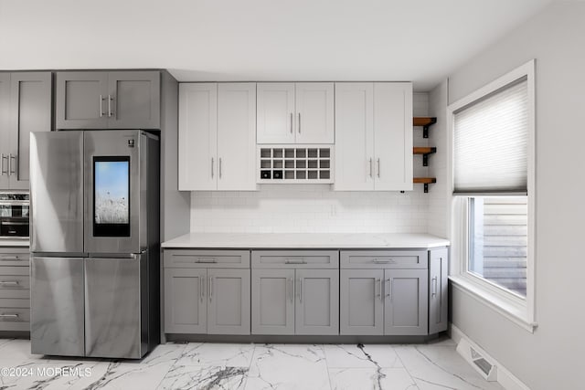 kitchen with stainless steel fridge, light stone countertops, gray cabinetry, and tasteful backsplash