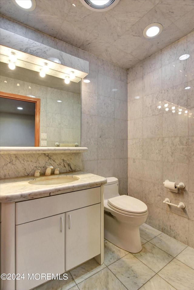 bathroom with tile walls, vanity, toilet, and tile patterned flooring