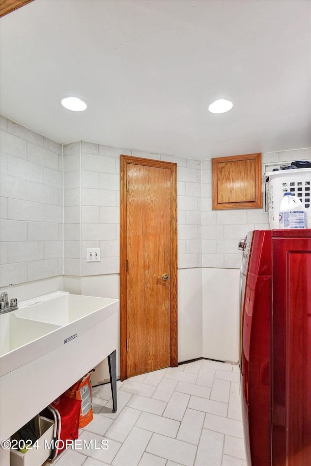 clothes washing area with sink, tile walls, cabinets, and washer and clothes dryer