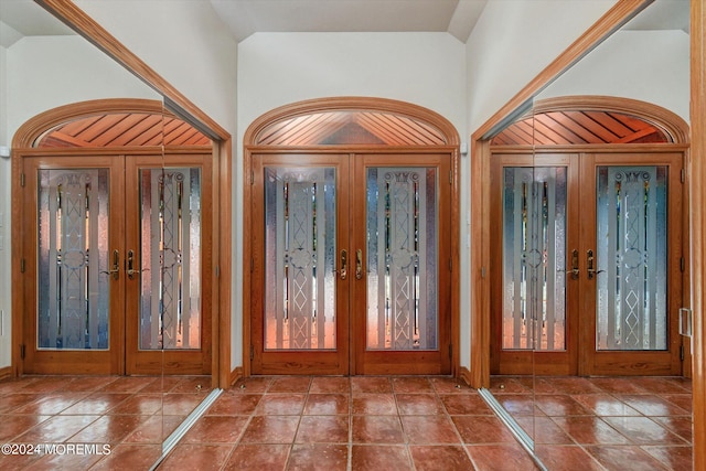 foyer with french doors, tile patterned flooring, wooden walls, and vaulted ceiling