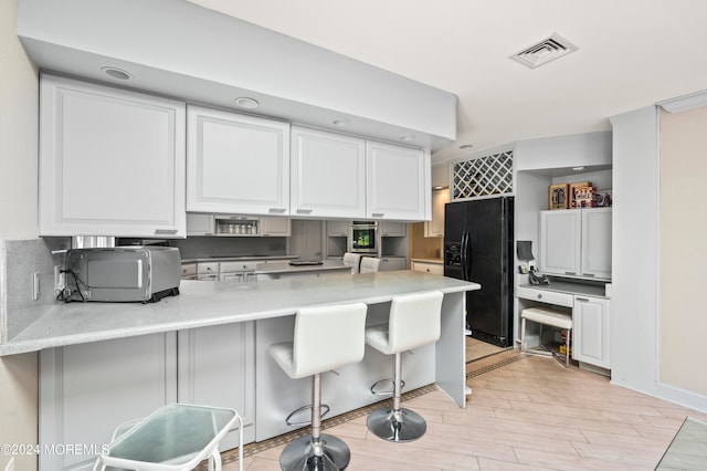 kitchen with black refrigerator with ice dispenser, kitchen peninsula, a kitchen breakfast bar, white cabinets, and light hardwood / wood-style flooring