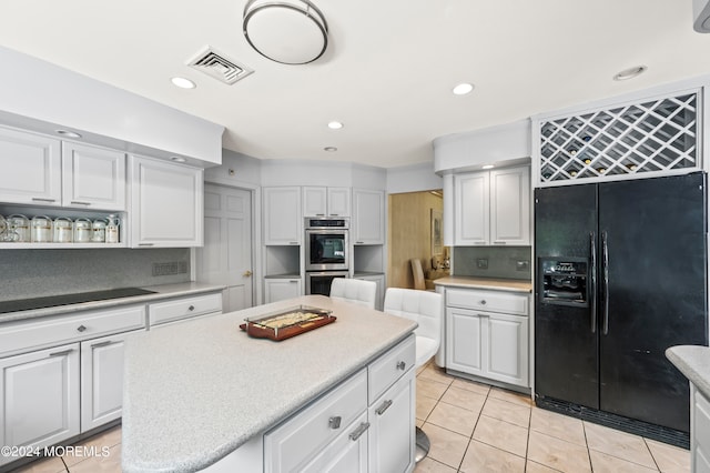 kitchen featuring double oven, a kitchen island, black fridge, and white cabinets