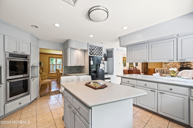 kitchen with double oven, light tile patterned flooring, a kitchen island, and black fridge with ice dispenser