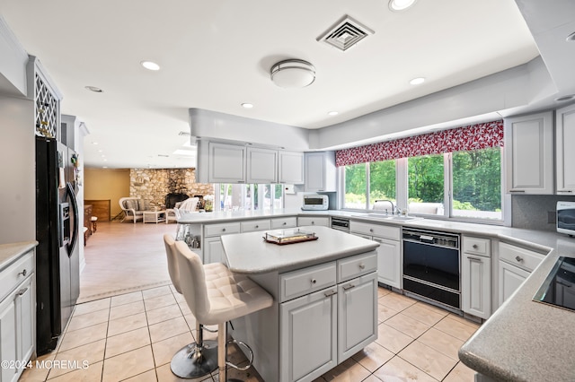 kitchen featuring a breakfast bar area, sink, black appliances, a center island, and light tile patterned floors