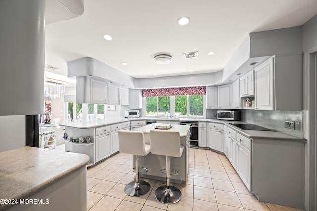 kitchen with white cabinets, light tile patterned floors, a breakfast bar, black appliances, and a center island