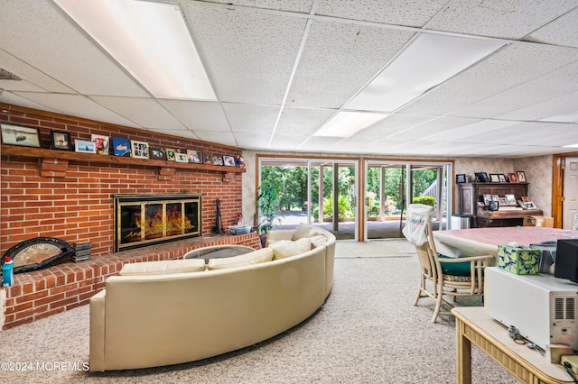 living room with a drop ceiling, carpet flooring, and a brick fireplace