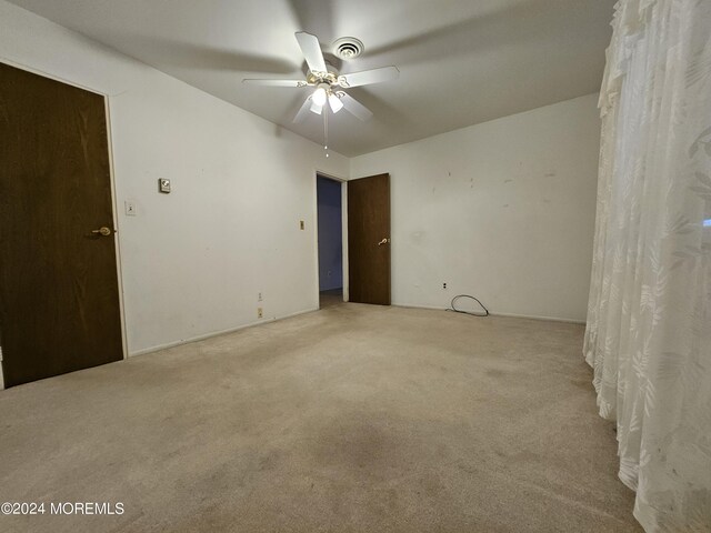 empty room featuring visible vents, a ceiling fan, and carpet flooring