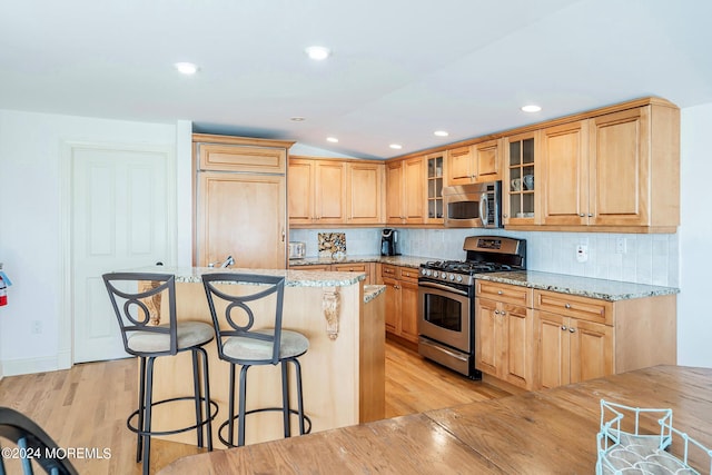 kitchen featuring appliances with stainless steel finishes, light stone counters, backsplash, and light hardwood / wood-style floors