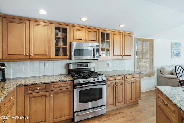 kitchen with light stone countertops, stainless steel appliances, light hardwood / wood-style floors, and tasteful backsplash