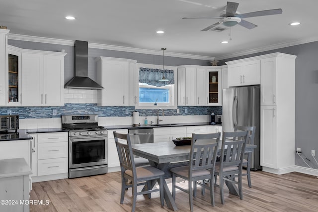 kitchen featuring wall chimney range hood, light hardwood / wood-style flooring, hanging light fixtures, stainless steel appliances, and sink