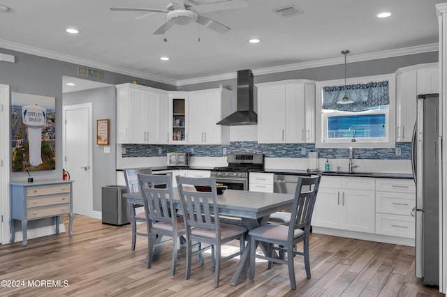 kitchen featuring sink, light hardwood / wood-style floors, stainless steel appliances, wall chimney exhaust hood, and pendant lighting