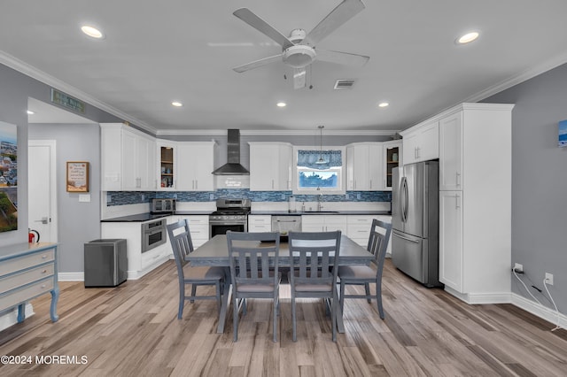 kitchen featuring sink, light wood-type flooring, stainless steel appliances, wall chimney exhaust hood, and white cabinets