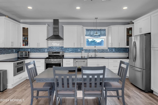 kitchen with light hardwood / wood-style flooring, stainless steel appliances, wall chimney exhaust hood, and decorative light fixtures