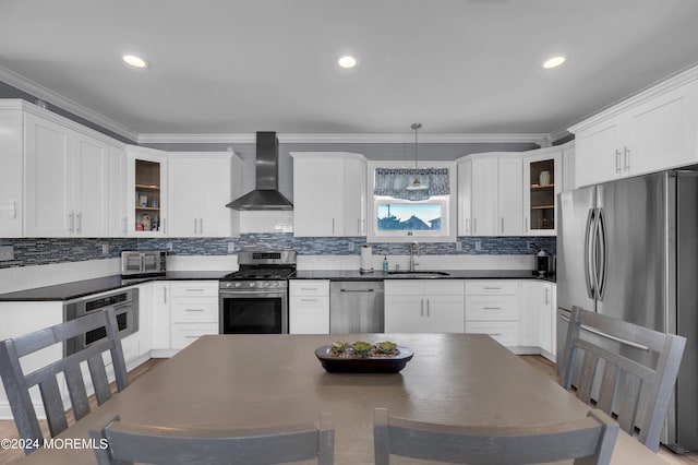 kitchen featuring wood-type flooring, sink, stainless steel appliances, wall chimney exhaust hood, and decorative light fixtures