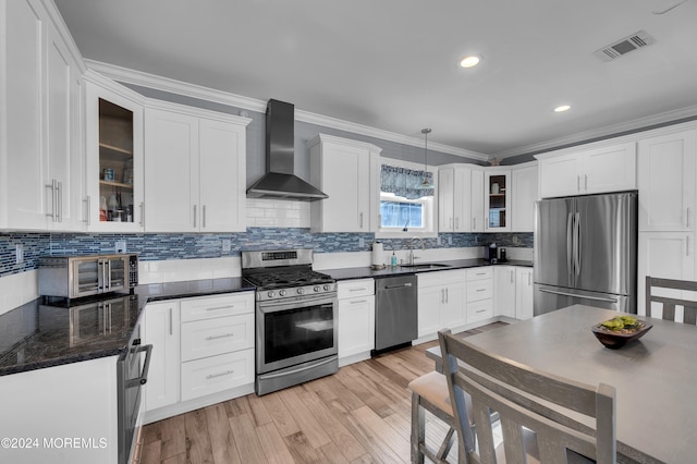 kitchen featuring appliances with stainless steel finishes, light hardwood / wood-style floors, wall chimney exhaust hood, decorative light fixtures, and ornamental molding