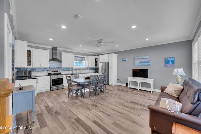 kitchen featuring wall chimney range hood, crown molding, white cabinets, appliances with stainless steel finishes, and light hardwood / wood-style floors