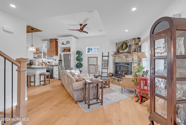 living room with light wood-type flooring, crown molding, ceiling fan, and a fireplace