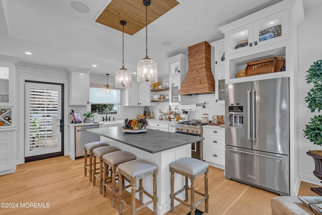 kitchen with a kitchen breakfast bar, light hardwood / wood-style flooring, white cabinets, premium appliances, and premium range hood