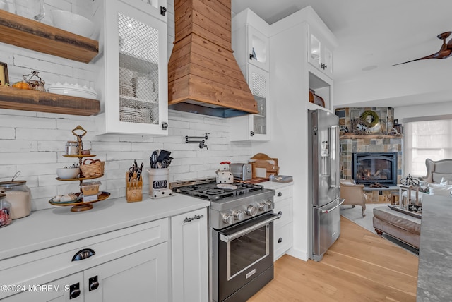 kitchen featuring a stone fireplace, light wood-type flooring, custom range hood, premium appliances, and white cabinets