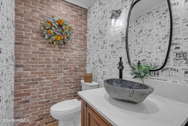 bathroom with toilet, vanity, and brick wall