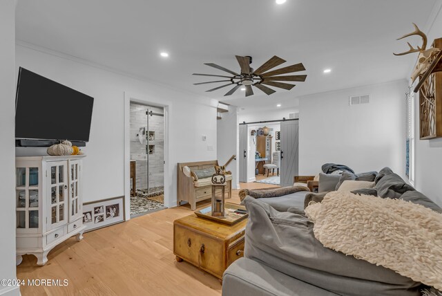 living room with a barn door, hardwood / wood-style flooring, ceiling fan, and ornamental molding