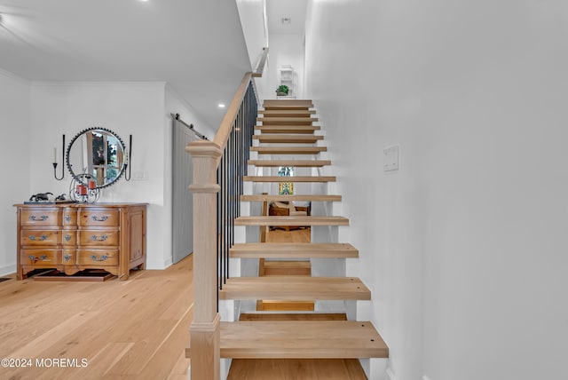 stairway with a barn door, hardwood / wood-style flooring, and ornamental molding