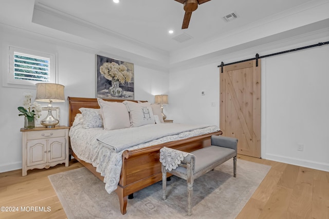 bedroom with crown molding, a barn door, ceiling fan, and light hardwood / wood-style flooring