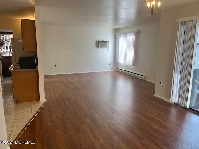 unfurnished living room with a baseboard radiator, a wall mounted AC, wood-type flooring, and an inviting chandelier