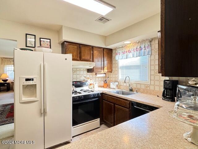 kitchen with a sink, gas range oven, under cabinet range hood, white fridge with ice dispenser, and backsplash