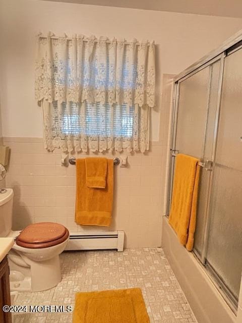 bathroom featuring toilet, combined bath / shower with glass door, tile walls, a baseboard radiator, and vanity