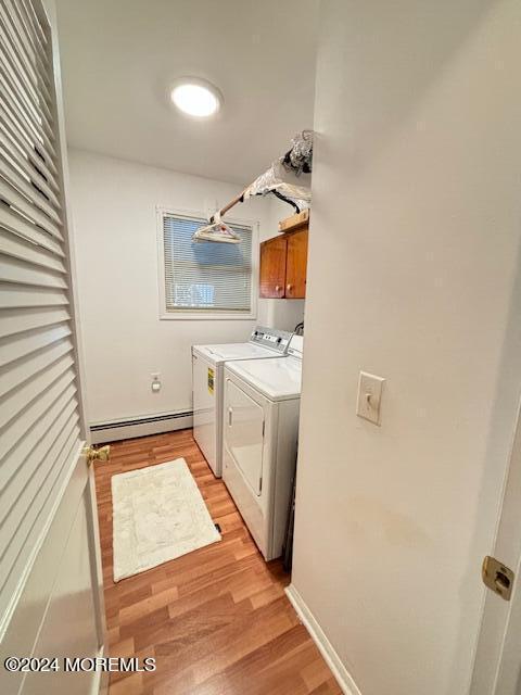 clothes washing area with a baseboard heating unit, light wood-style flooring, washer and dryer, and cabinet space