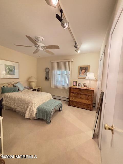 bedroom featuring a baseboard radiator, ceiling fan, rail lighting, a closet, and light colored carpet