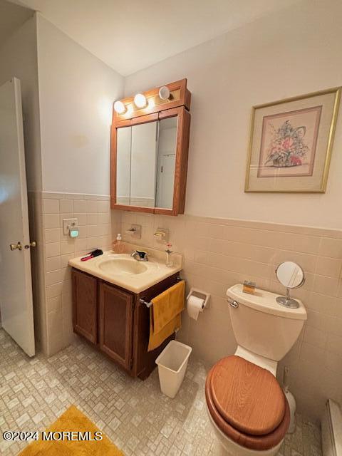 half bathroom with vanity, toilet, tile walls, and wainscoting