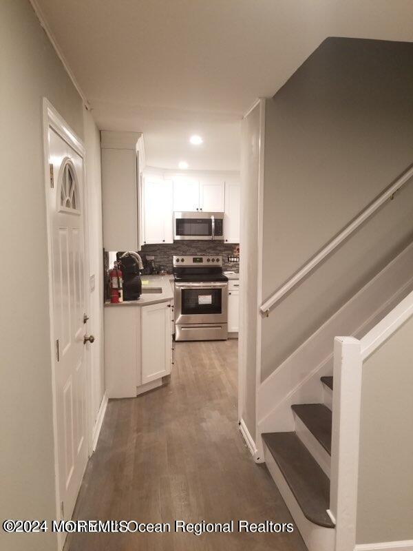 kitchen with appliances with stainless steel finishes, decorative backsplash, hardwood / wood-style flooring, and white cabinetry