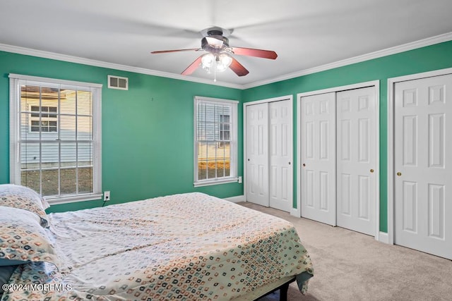 carpeted bedroom with ornamental molding, two closets, and ceiling fan