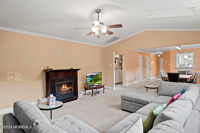 carpeted living room with vaulted ceiling with skylight, crown molding, washer and clothes dryer, and ceiling fan