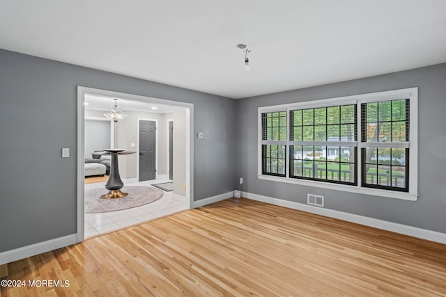 empty room featuring a notable chandelier and light wood-type flooring