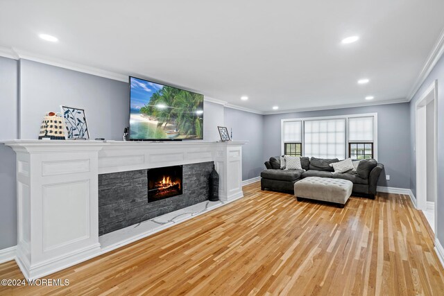 living room featuring crown molding, a stone fireplace, and light wood-type flooring