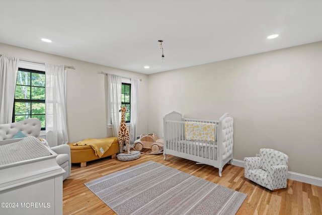 bedroom with light hardwood / wood-style flooring, multiple windows, and a crib