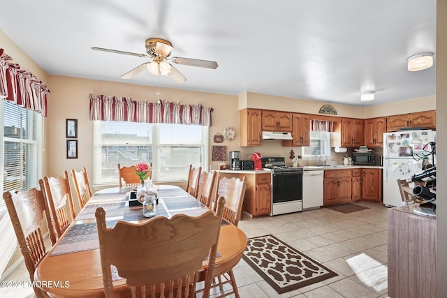 kitchen with a sink, under cabinet range hood, ceiling fan, white appliances, and light countertops