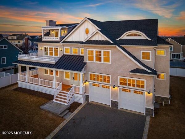 shingle-style home featuring driveway, a balcony, metal roof, a standing seam roof, and a porch