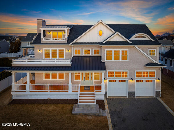 shingle-style home featuring a porch, an attached garage, a balcony, driveway, and a standing seam roof