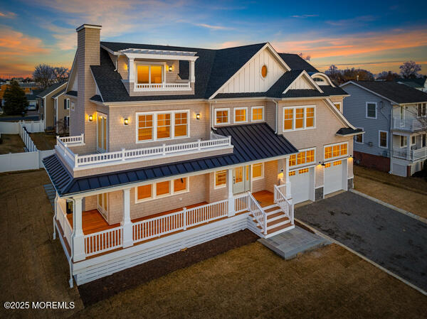 back of house at dusk with driveway, a balcony, a standing seam roof, a porch, and board and batten siding